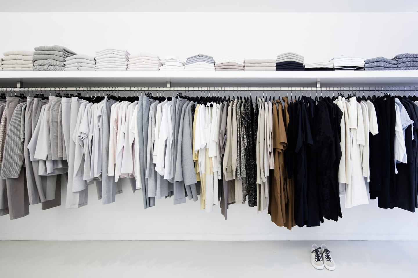 Rek met kleding in wit, grijs en zwart, met gevouwen breigoed op de plank erboven
